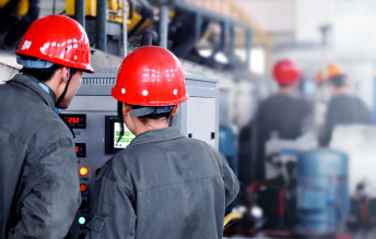 Factory worker in red helmet operating CNC lathe producing durable bearing housings and hydraulic valves for 24/7 industrial use.